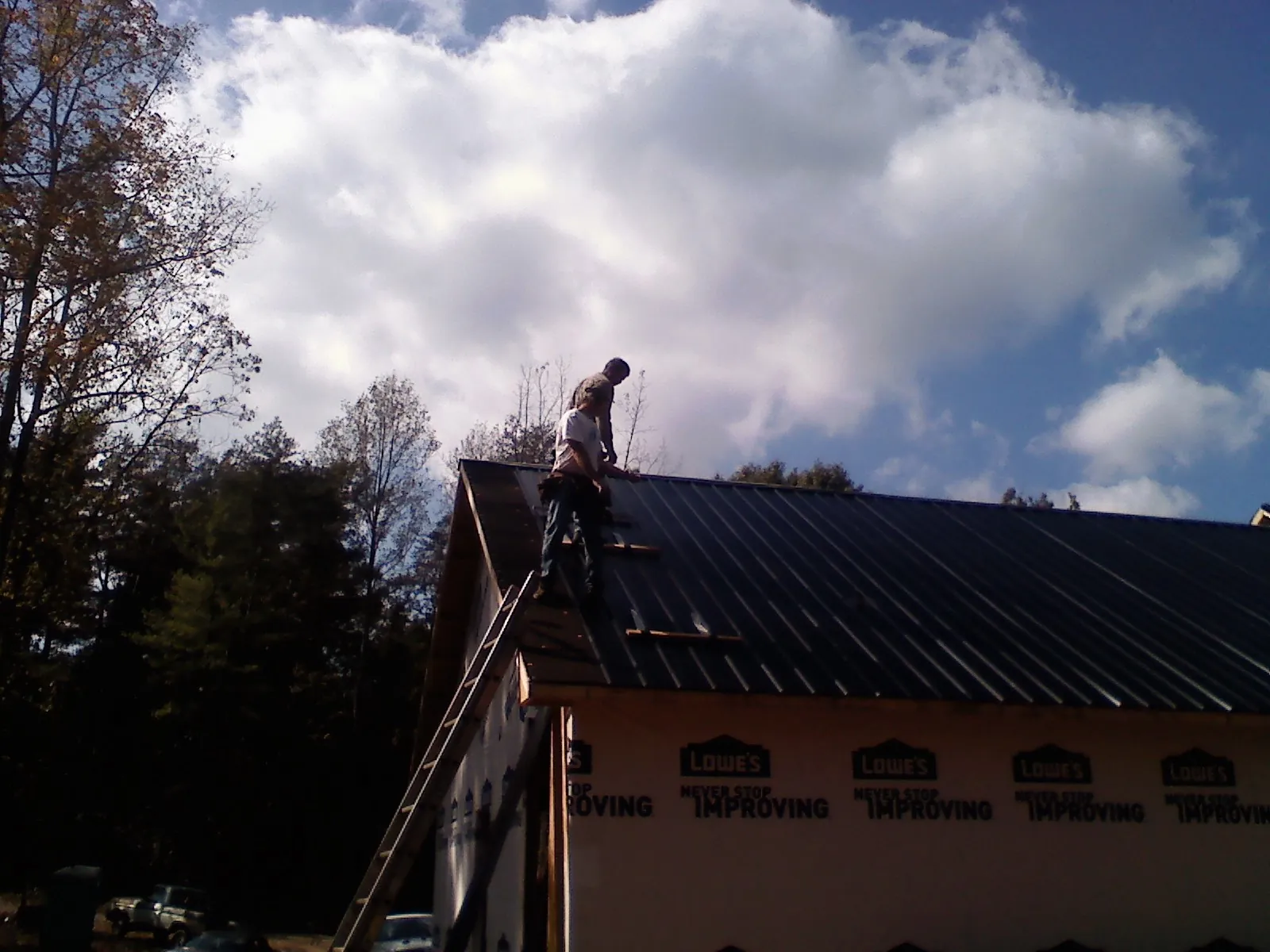 Roofer fastening dark metal panels high against a cloudy sky, from a Roof Inspection job in Wadmalaw Island