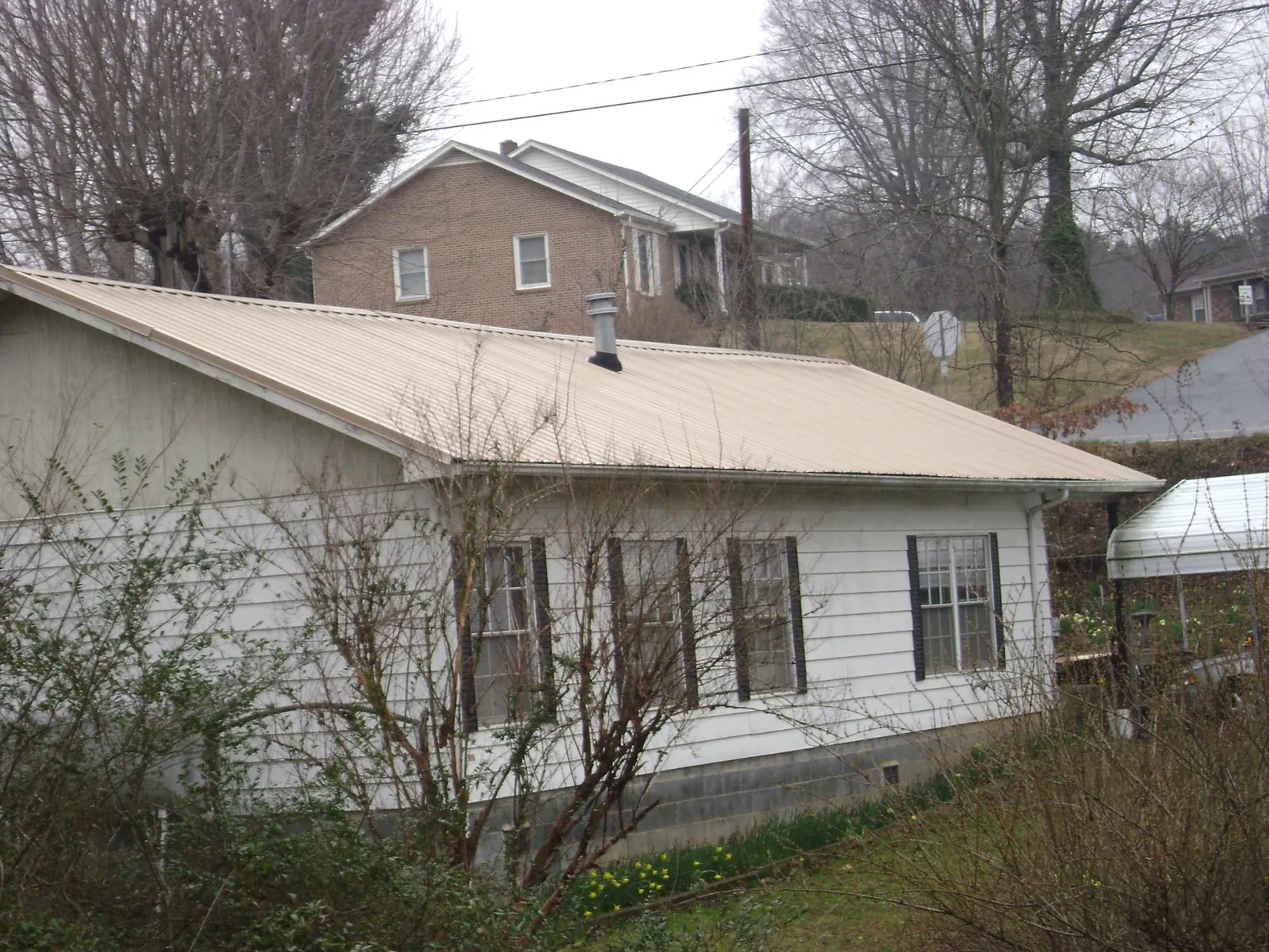 Tan metal roof on a white sided house set into a hillside — Commercial Roofing by Roofing Brothers in Wadmalaw Island
